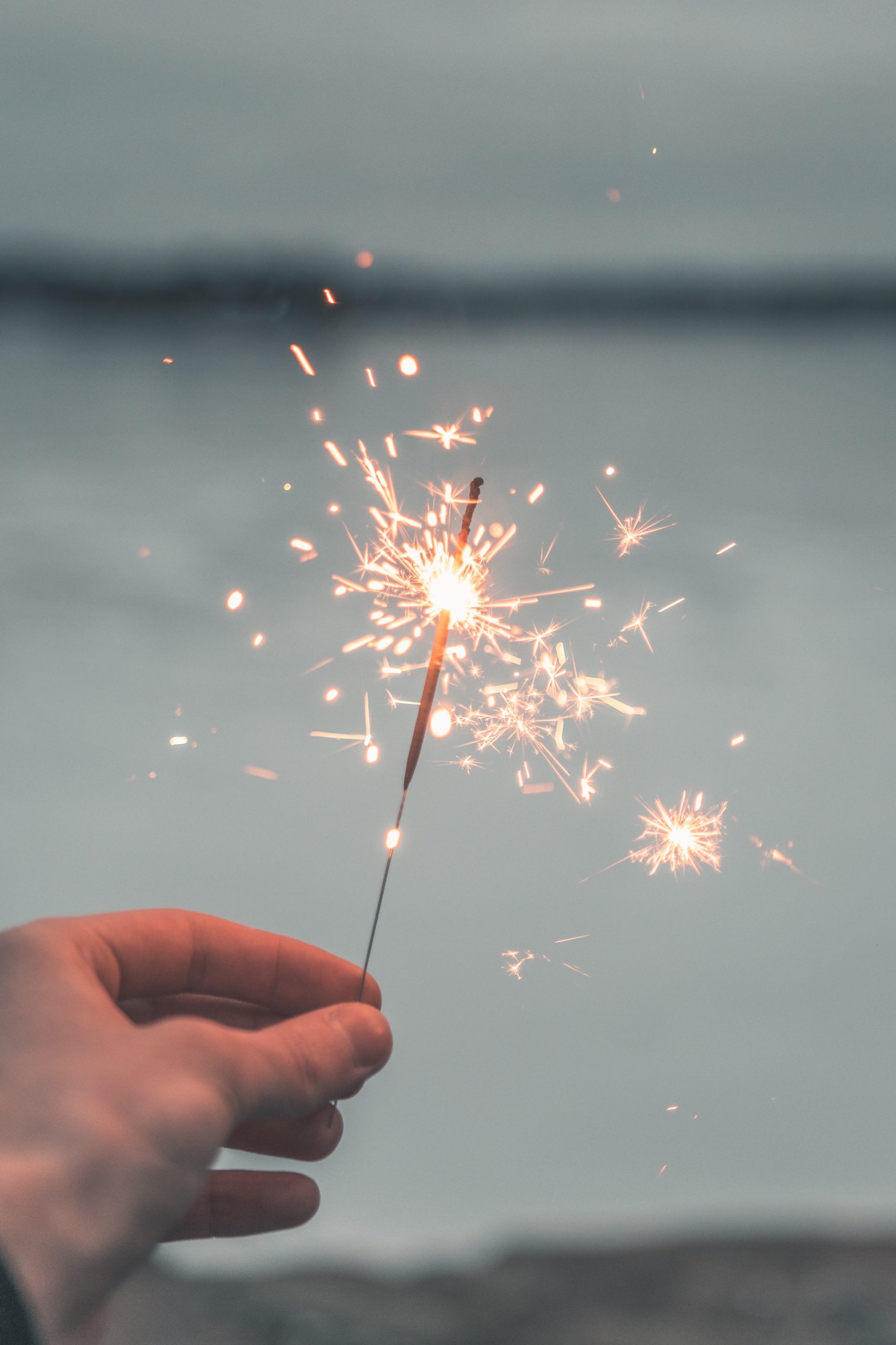 man's hand holding lit sparkler at twilight with blurred background