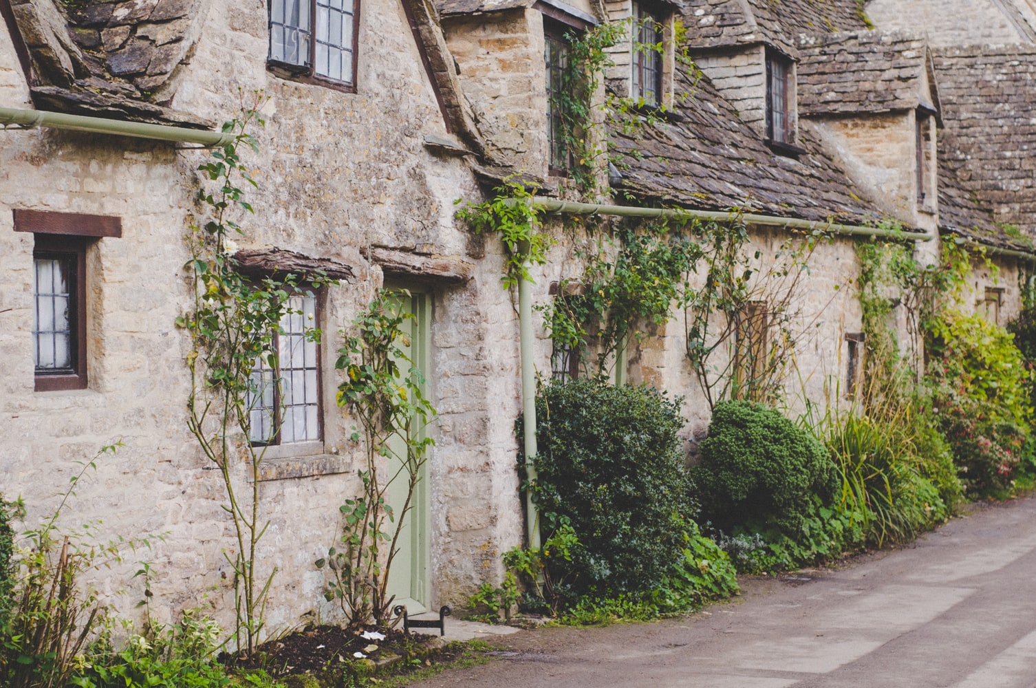 image showing row of english stone cottages with charming plantings in front and sage green trim