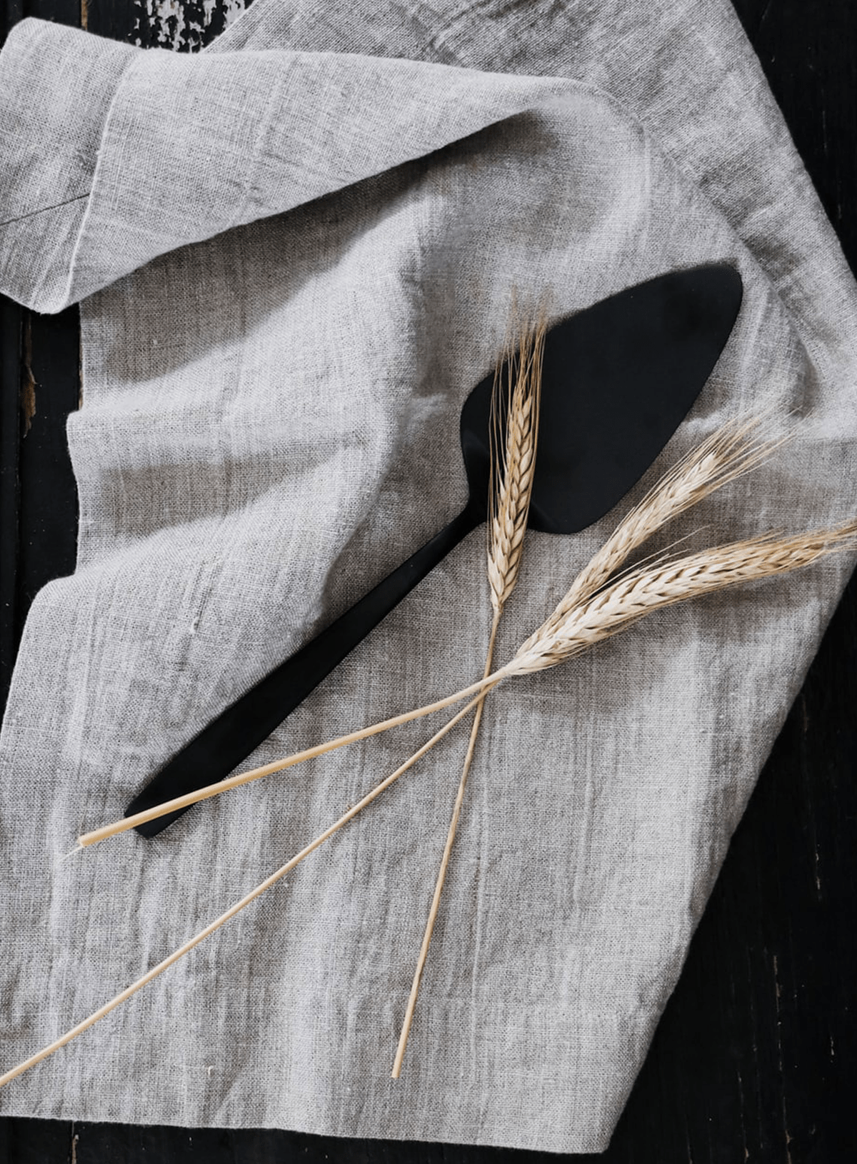 three stalks of wheat laying on a rustic linen napkin next to a pie server with a black finish