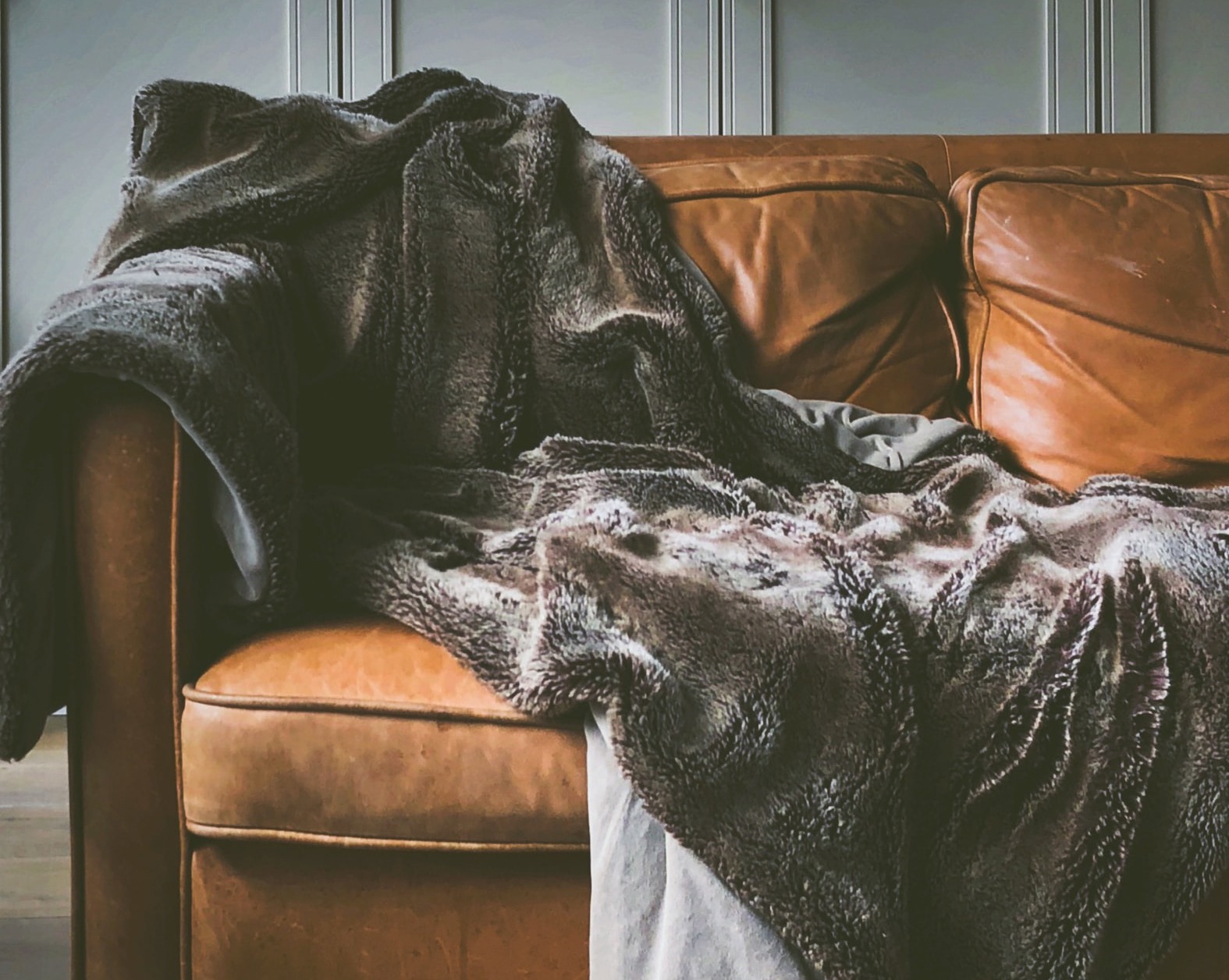 image of faux fur blanket on cognac leather sofa in front of grey paneled door