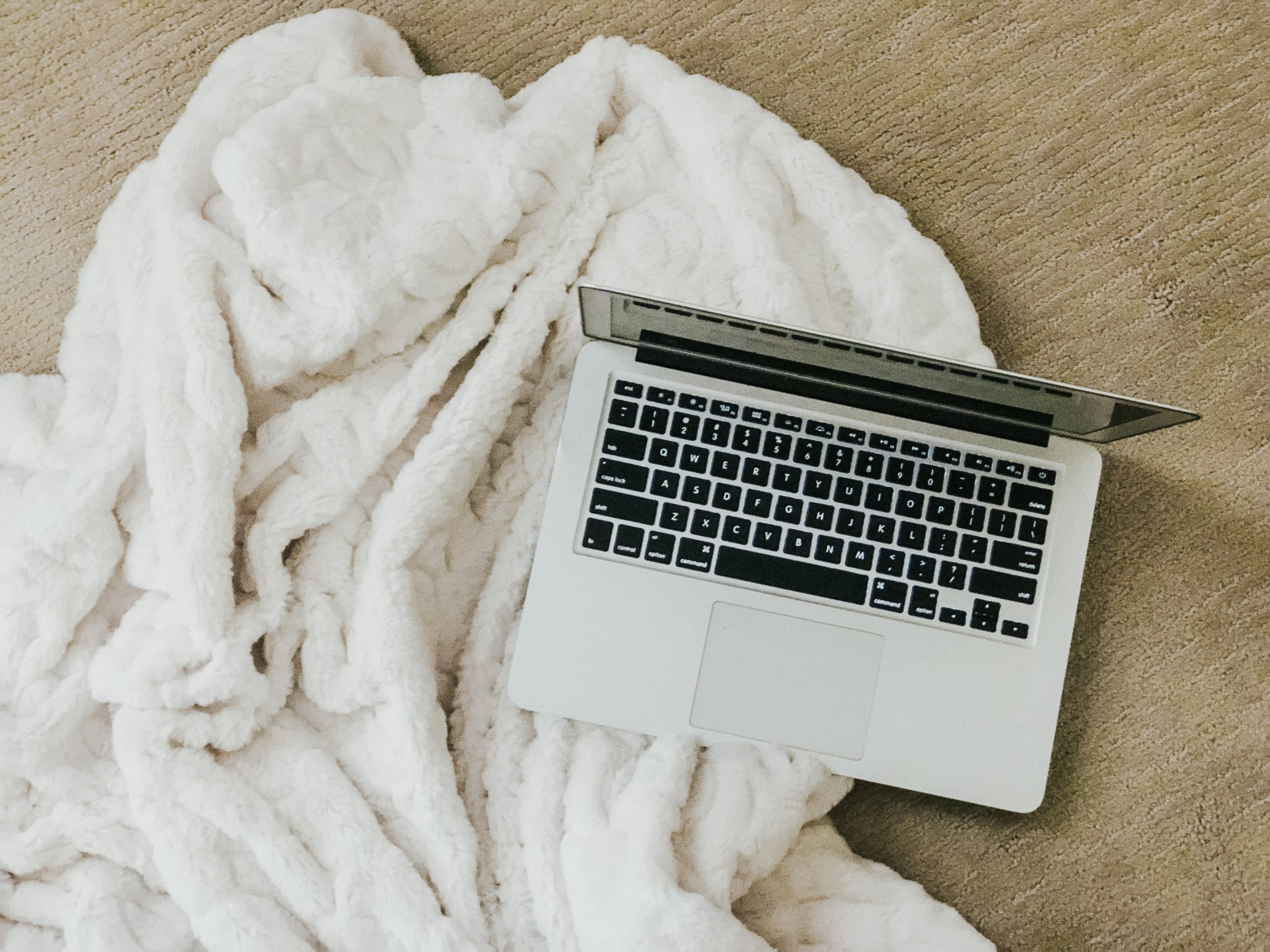 image of open laptop sitting on cozy white blanked on carpeted floor showing how to stay at home