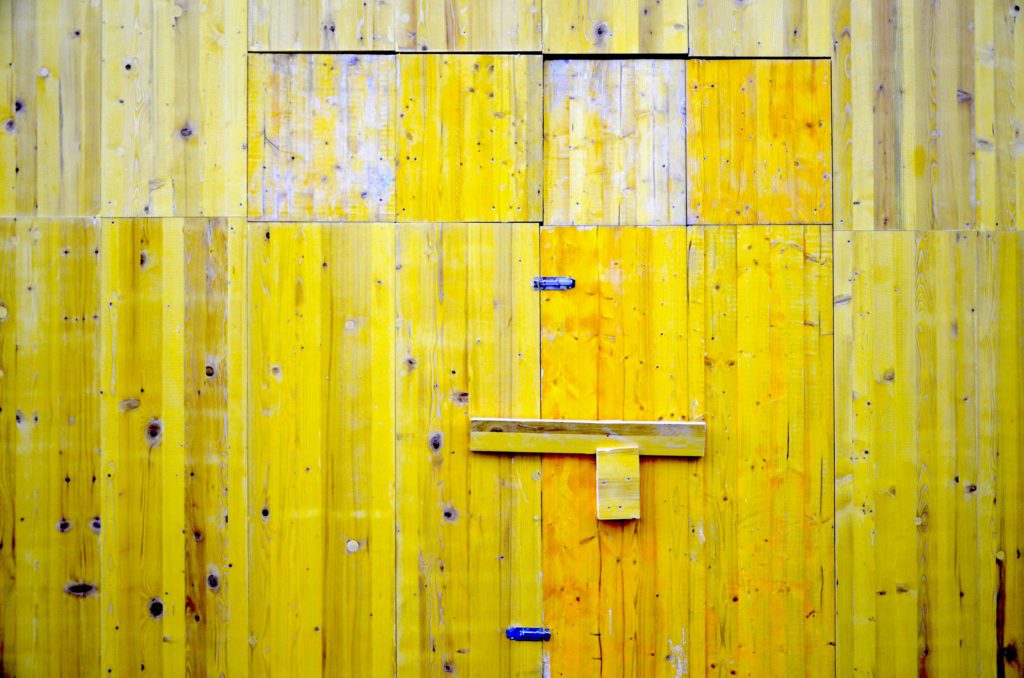 image of barn siding painted vibrant yellow but with weathered sections