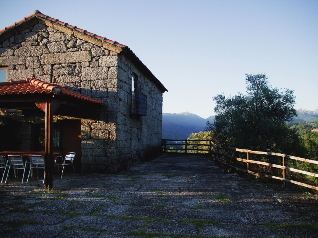 photo of a stone farmhouse with a tile roof, next to a stone paver road