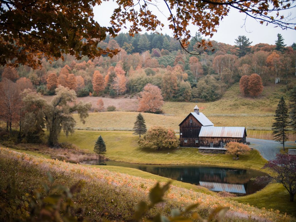 photo of a barn and farmhouse nestled in a valley with fall trees surrounding it