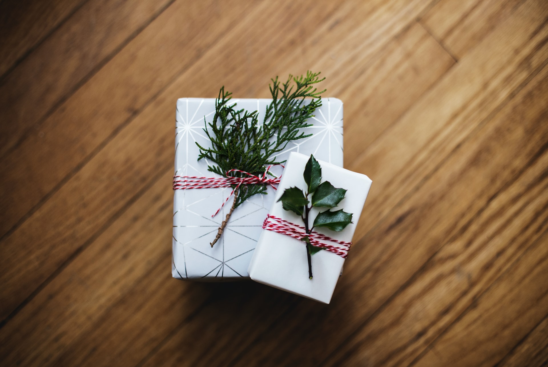 white packages wrapped with red string with a sprig of holly tucked into the string on top of a warm wooden floor
