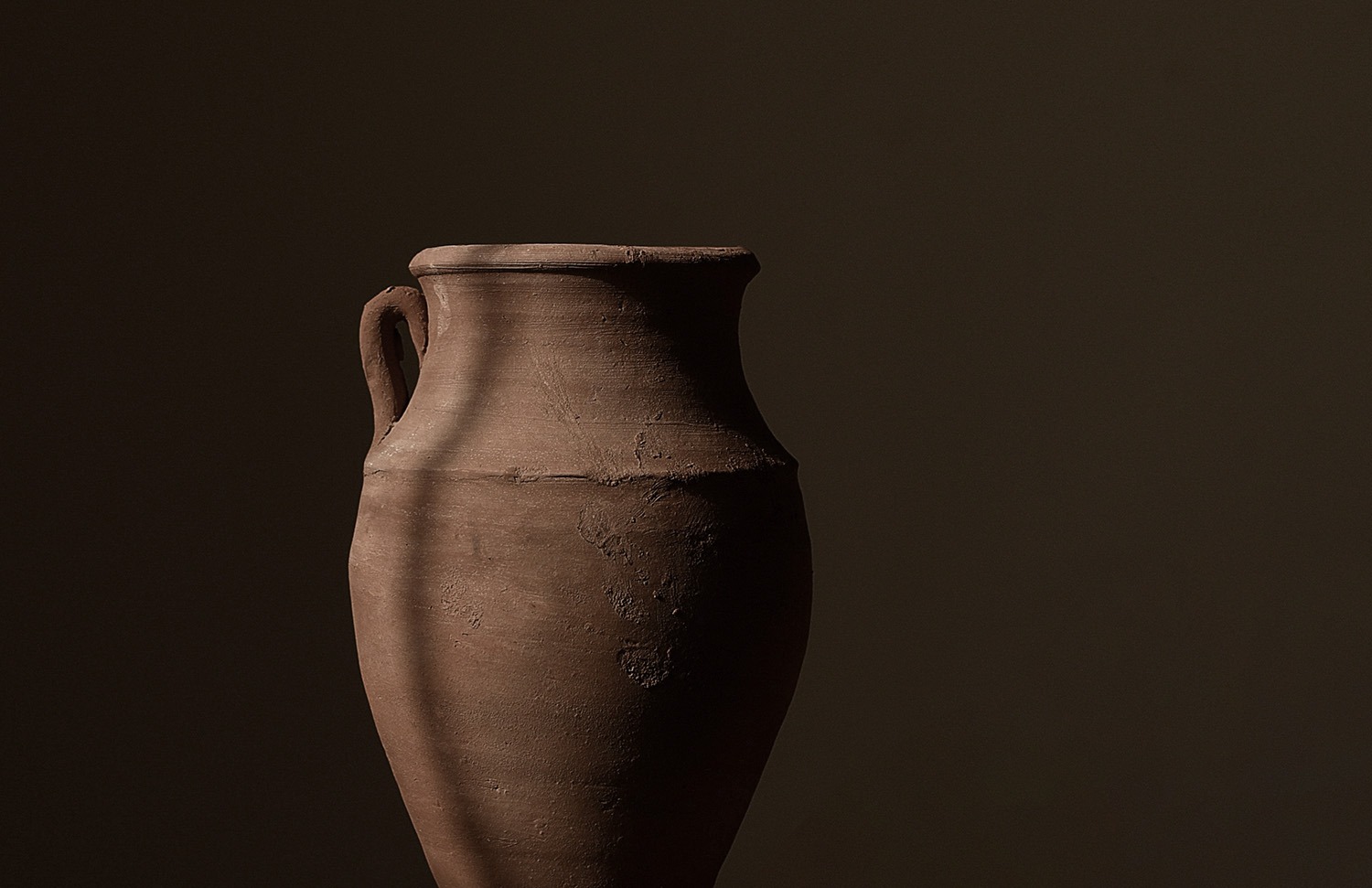 a weathered pottery urn in front of a brown painted wall