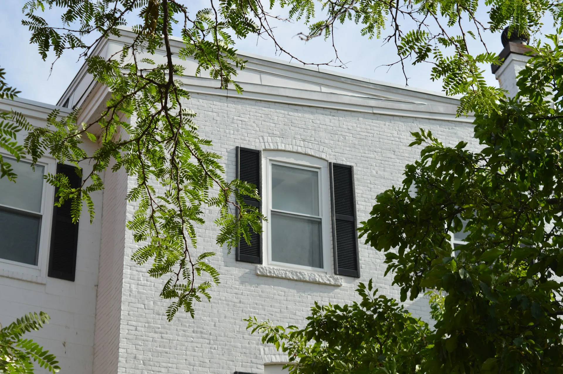 white brick house with black shutters surrounded by green trees