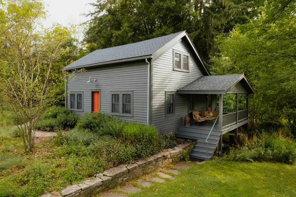 a traditional cape cod painted dark charcoal with a bright coral door