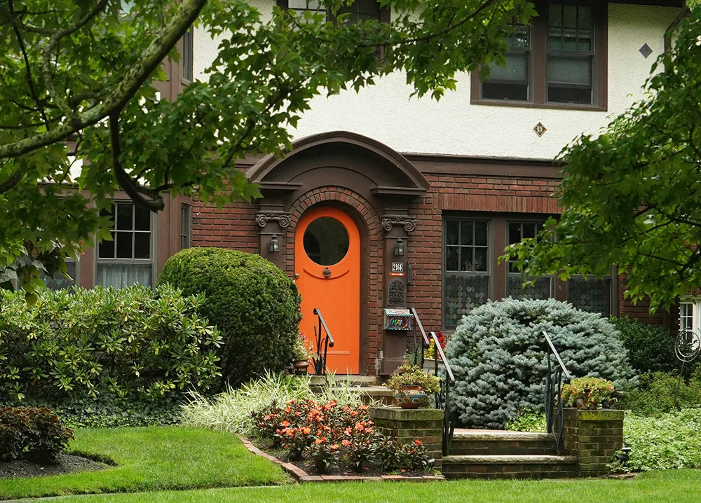 A tudor house with a bright orange door with a round =window