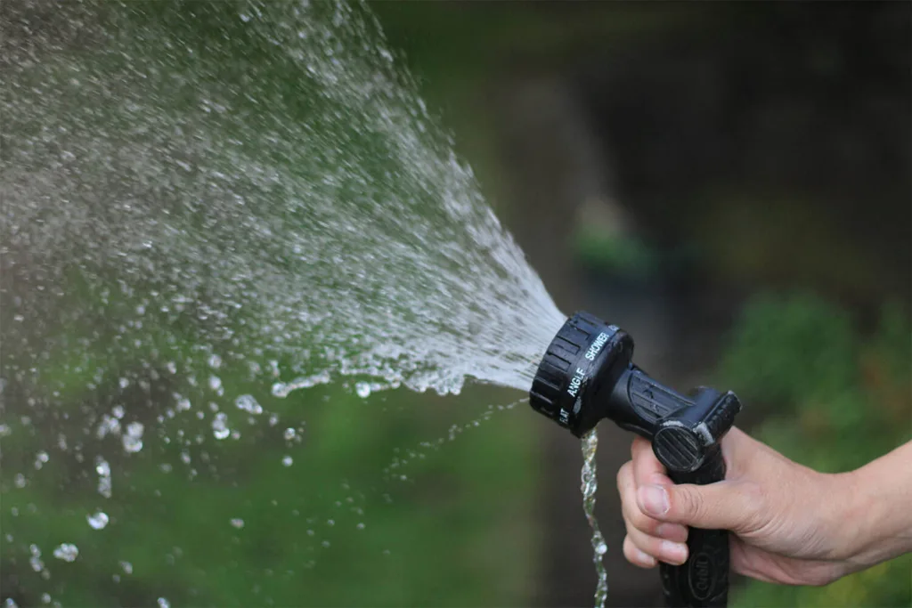 a hand holding a hose sprayer with water spraying out of it over a green background